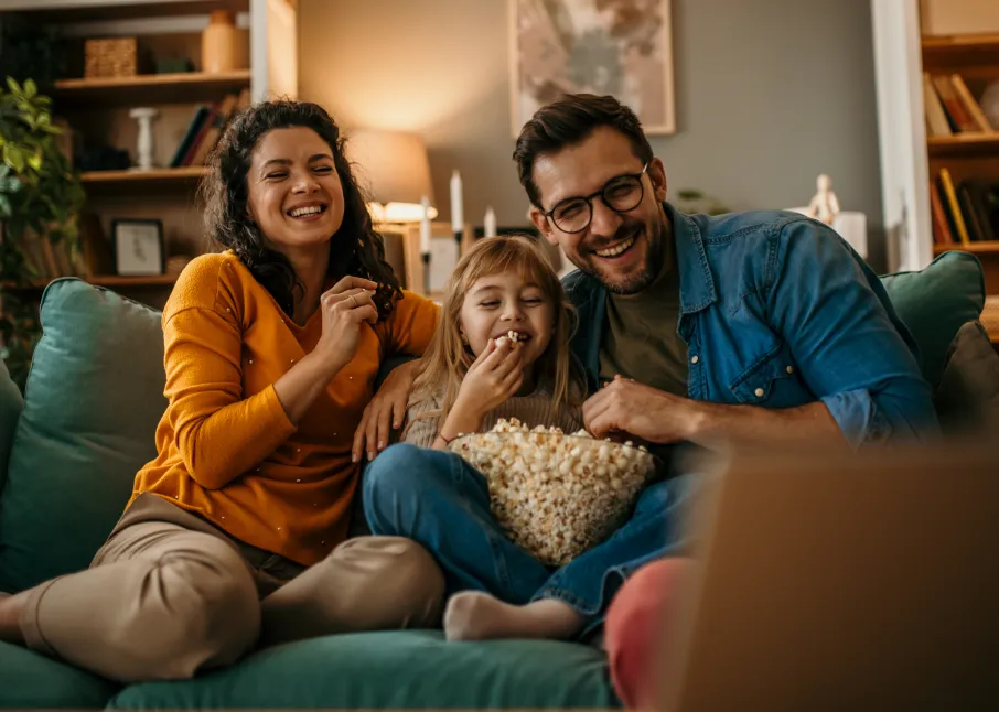 Couple on the couch snuggling their child and enjoying a movie with popcorn.