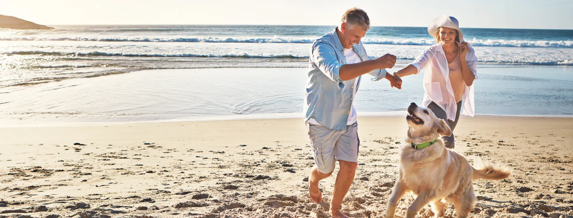 Older couple playing with their dog on a sunset lit beach.